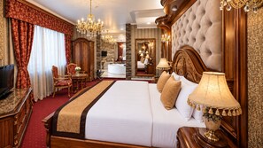 Une chambre d’hôtel dotée d’un grand lit, d’un coin salon avec un fauteuil et une table, d’une télévision et d’une salle de bain avec un miroir et un lavabo.