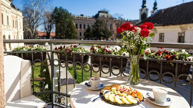 A balcony with a table set for a meal, a vase with flowers, and a view of historic buildings.