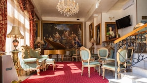 A grand room with a red carpet, ornate furniture, a grand piano, and a staircase with intricate metalwork.