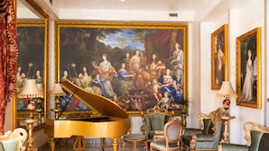 A grand room with a grand piano, ornate chairs, and a large classical painting on the wall.
