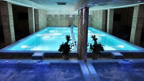 A large indoor swimming pool with clear water, surrounded by stone walls and tiled flooring.