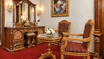A room with a wooden dresser, a mirror, a round table with a vase of flowers, a red upholstered chair, and a framed painting on the wall.