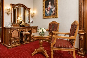 Une pièce comprenant une commode en bois, un miroir, une table ronde ornée d’un vase de fleurs, un fauteuil rouge recouvert de tissu et un tableau encadré accroché au mur.