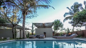 A pool area with lounge chairs and a covered seating area, surrounded by palm trees and a clear sky. - Liv Inn Guest House (Maputo)