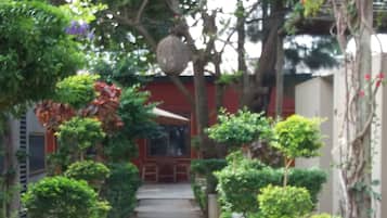 A pathway lined with greenery and small trees, leading to a building with a red facade.