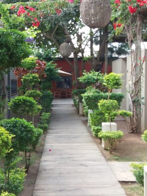 A pathway lined with greenery and small trees, leading to a building with a red facade.