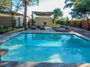 A swimming pool with lounge chairs and a covered seating area.