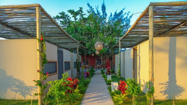 A covered walkway with a wooden floor, flanked by greenery and small plants. - Liv Inn Guest House (Maputo)