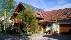 Una casa de madera tradicional con techo inclinado, instalación de paneles solares y un coche clásico estacionado al frente.