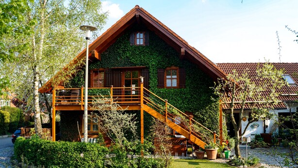 Ein Haus mit einer Holztreppe, die zu einem Balkon führt, umgeben von Grünpflanzen.
