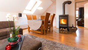 Ein gemütliches Wohnzimmer mit Holzboden, einem Esstisch mit Stühlen, einer Couch, einem Kamin und einem Oberlicht.