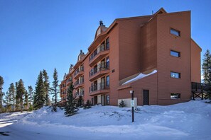 A multi-story building with balconies, surrounded by snow and trees.