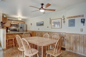 A kitchen with wooden cabinets, a dining table with chairs, a ceiling fan, and wall-mounted light fixtures.