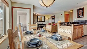 A dining area with a wooden table set for four, a kitchen with wooden cabinets, and a hanging light fixture. - 522 Watch Hill (Silverthorne)