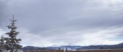 A view of a building complex with multiple brick structures, some with snow on the roofs, and a backdrop of snow-covered mountains under a cloudy sky.