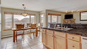 A kitchen with a granite countertop, wooden cabinets, a stone fireplace, and a dining area with a view of mountains. - 522 Watch Hill (Silverthorne)