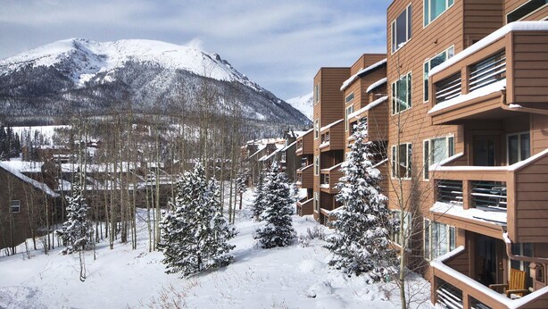 A modern multi-story building with balconies, surrounded by snow-covered trees and a mountain in the background. - 522 Watch Hill (Silverthorne)