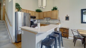A modern kitchen with wooden cabinets, a stainless steel refrigerator, a built-in oven, and a white island with bar stools.
