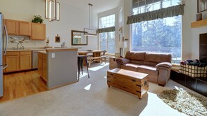 A spacious living area with a kitchen, wooden cabinets, a dining table, and a large window providing natural light.