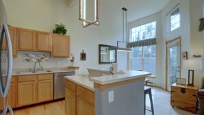 A modern kitchen with wooden cabinets, a central island, and a large window providing natural light.