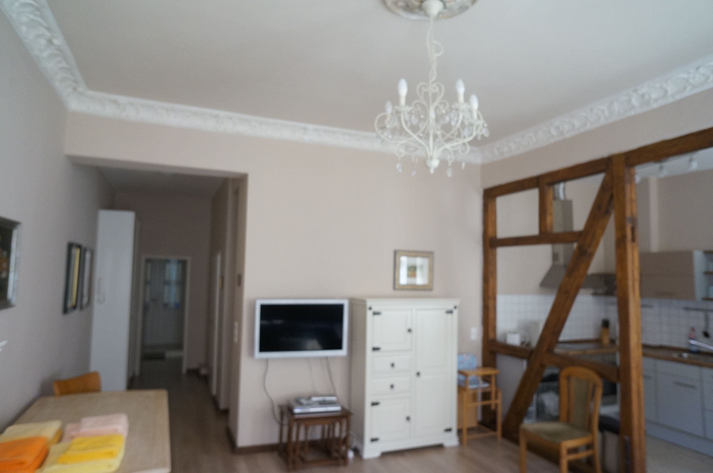 A room with a television, a white cabinet, a wooden chair, and a chandelier.
