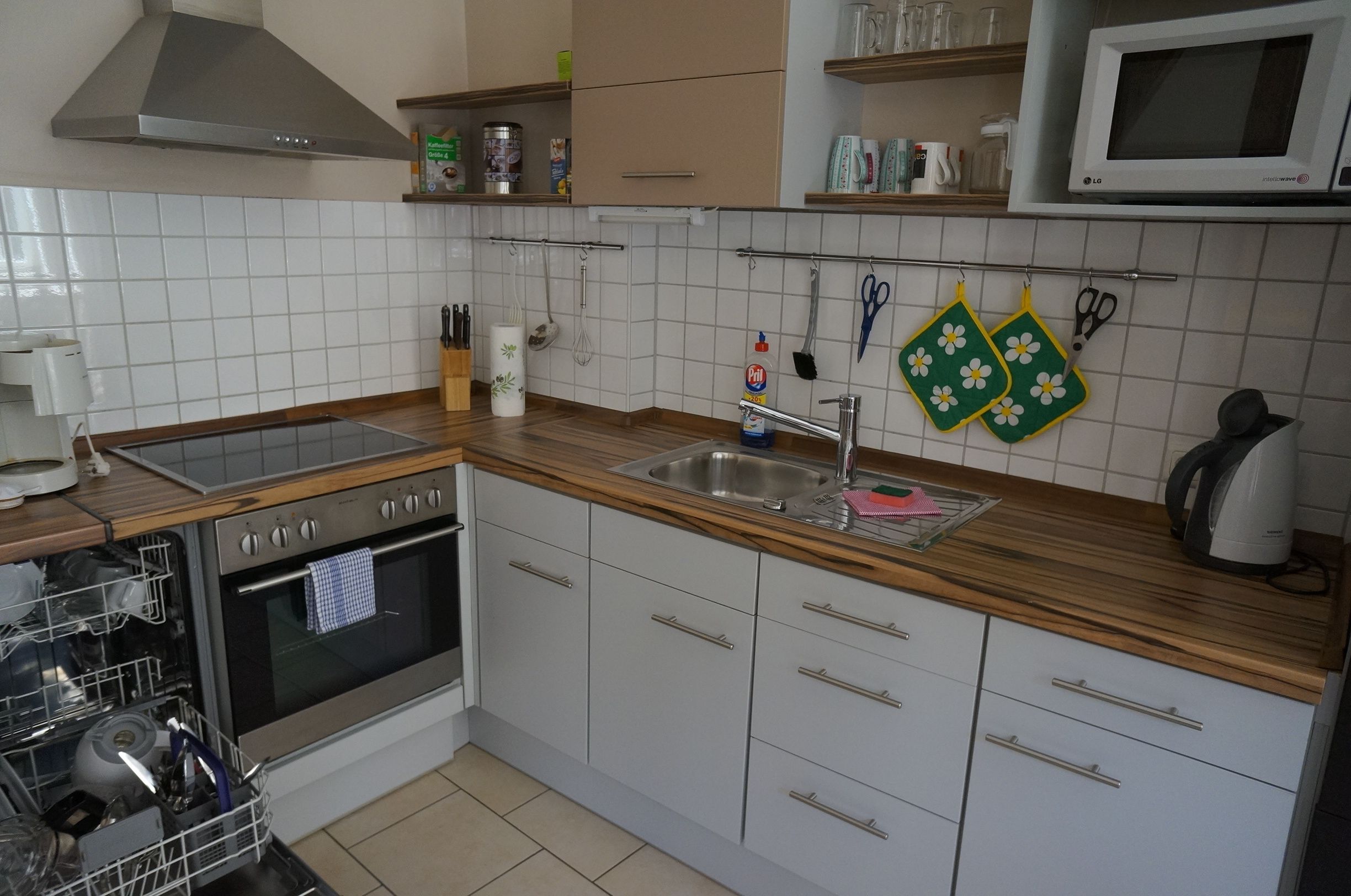 A kitchen with a stainless steel sink, wooden countertop, white cabinets, and a built-in oven.