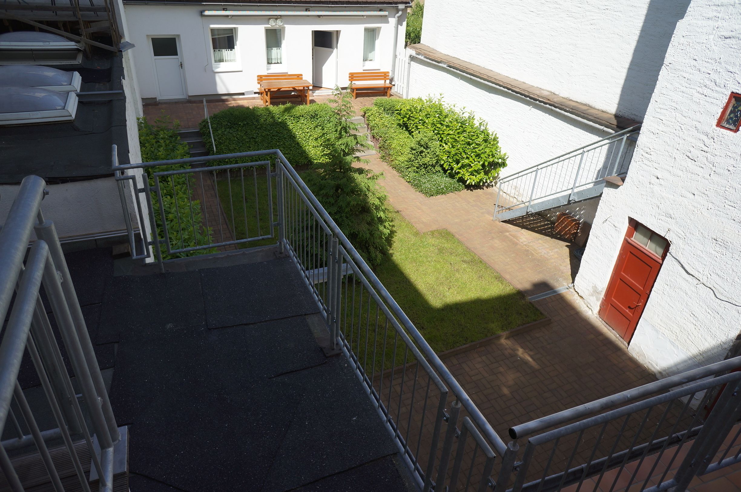 Vista desde un balcón sobre un patio con un banco de madera y una puerta.