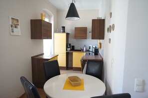 A compact kitchen with wooden cabinets, a dining table with chairs, and a hanging light fixture. - 3 wunderschöne Ferienwohnungen Kornhoff (Naumburg)