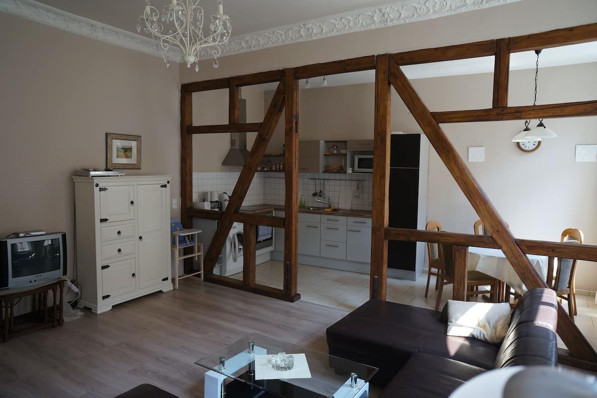 Ett rymligt vardagsrum med en modern soffa, ett soffbord i glas och en tv som står på ett litet stativ. I bakgrunden syns en matplats med ett bord i trä.