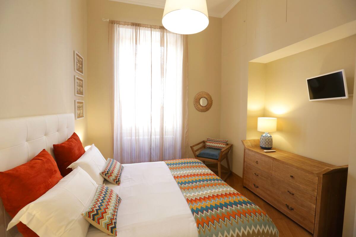 A bedroom with a bed, a chair, a dresser, and a television.