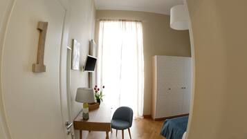 A room with a wooden desk, a chair, a bed with a blue blanket, a wardrobe, and a window with curtains.