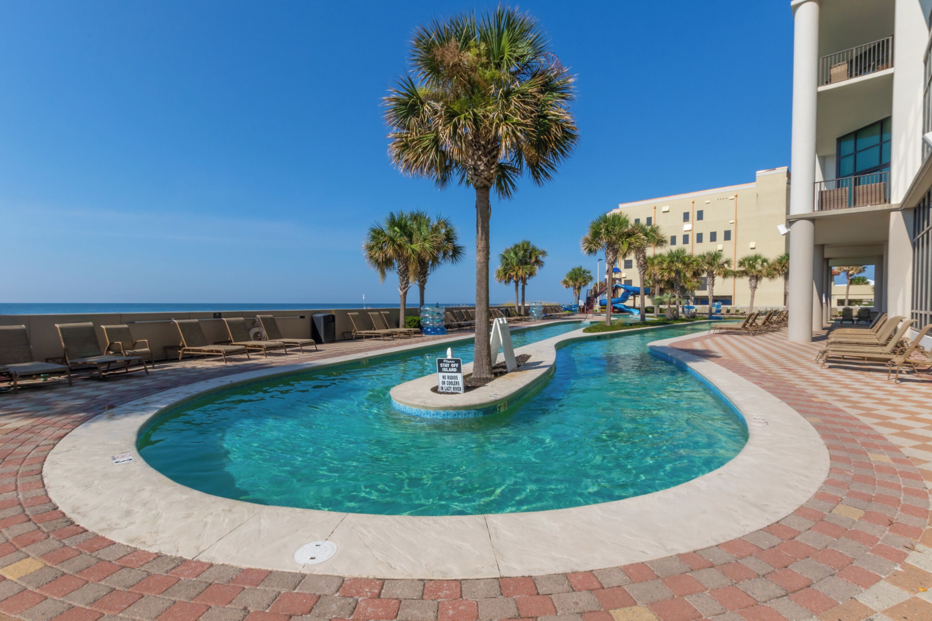 A pool area with palm trees, lounge chairs, and a view of the ocean.