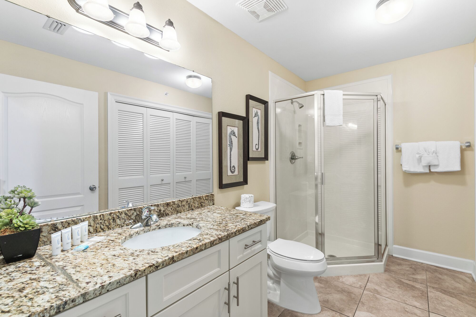 A bathroom with a granite countertop, a white sink, a toilet, a glass shower enclosure, and a large mirror.