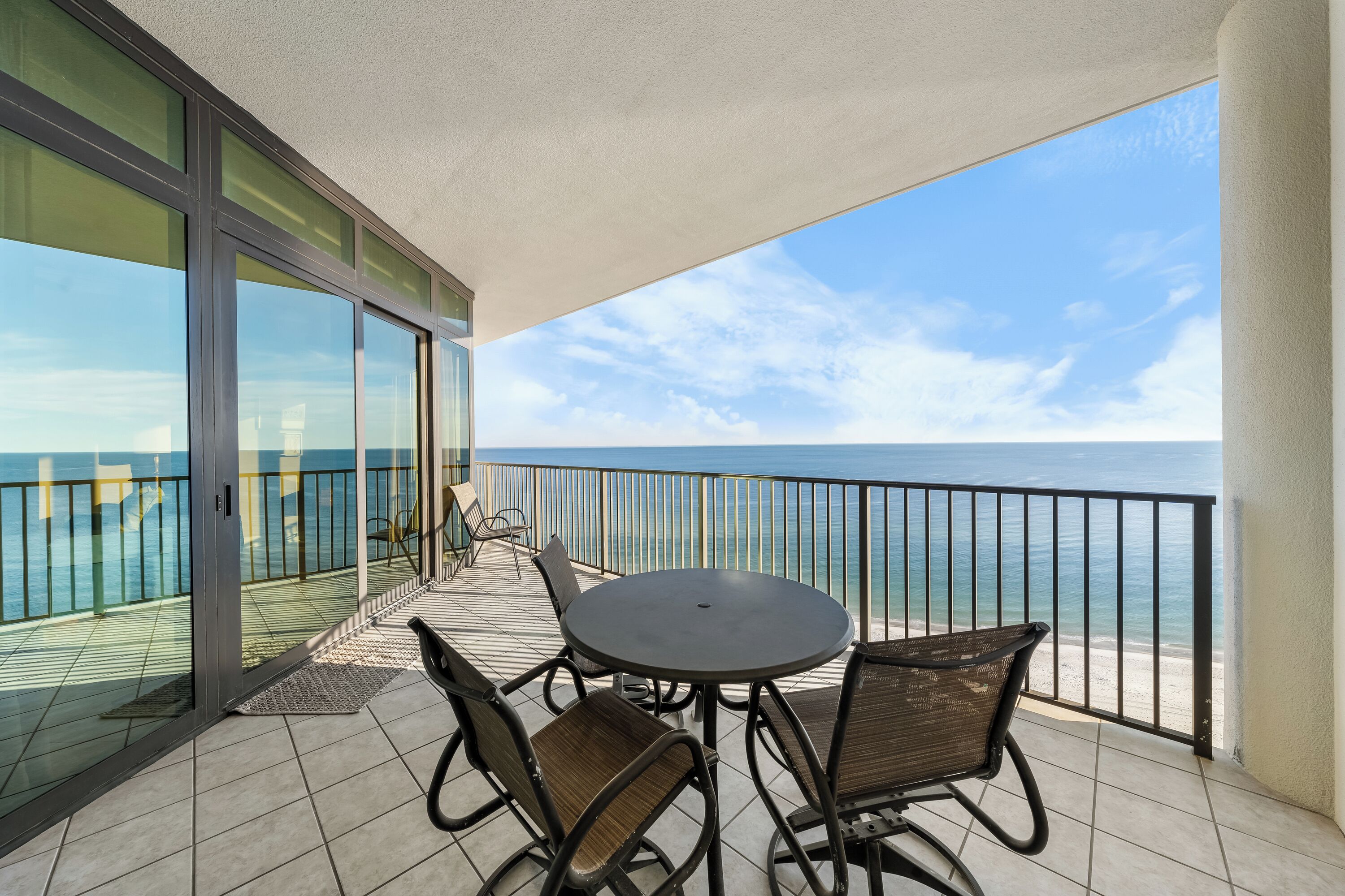 A balcony with a round table and chairs, overlooking a beach.