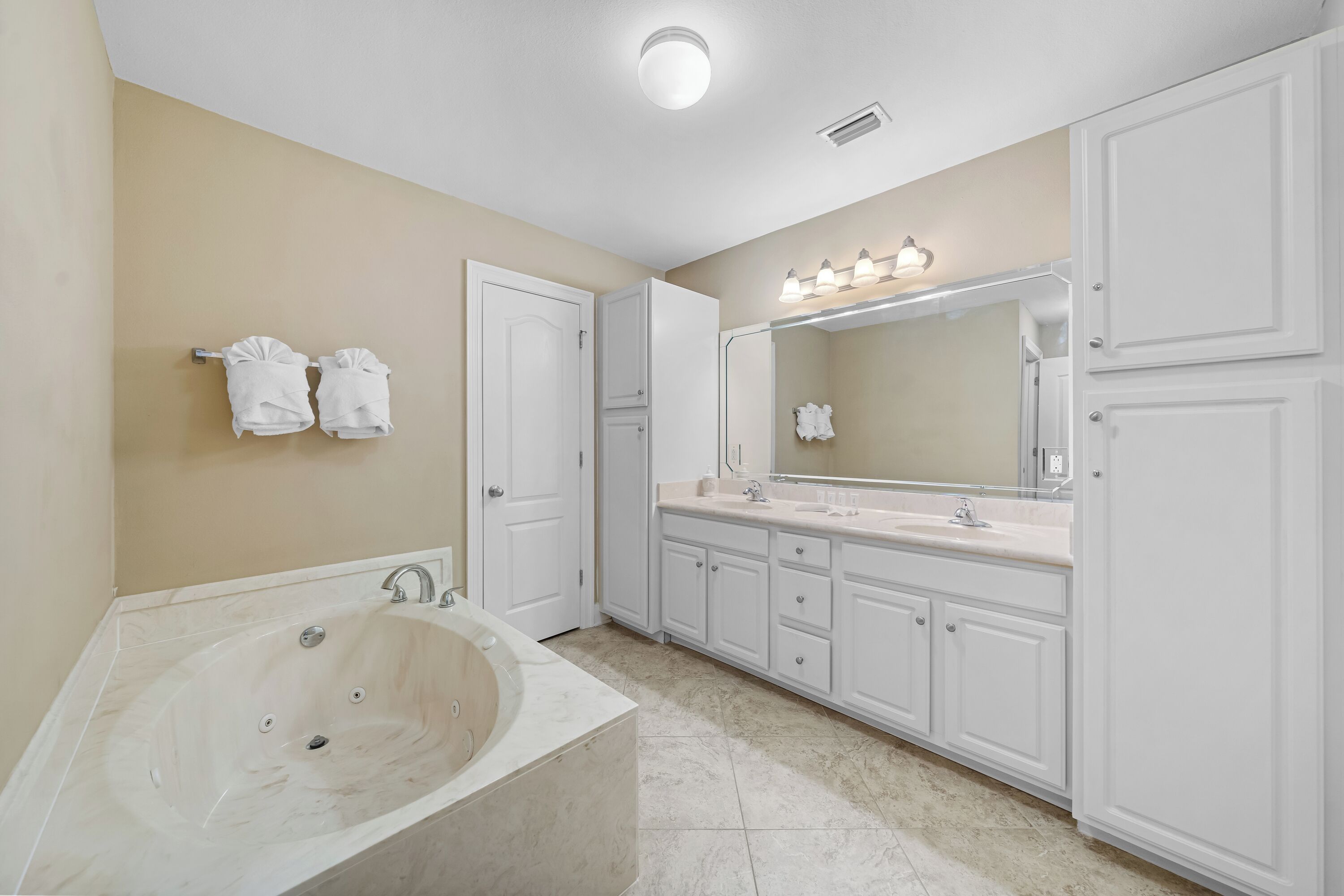 A bathroom with a large bathtub, white cabinets, and a vanity with a mirror.