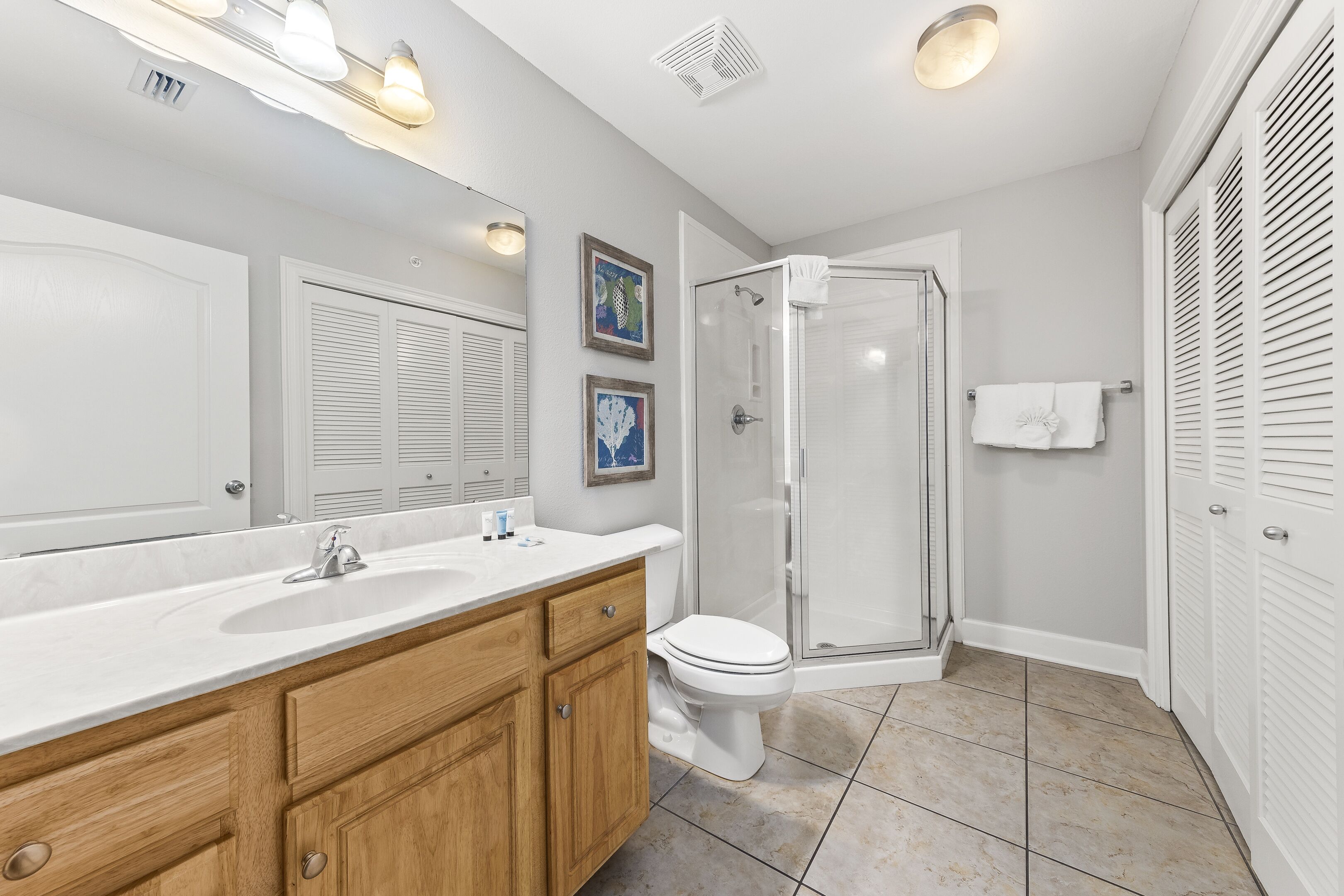 A modern bathroom with a large mirror, wooden vanity, white fixtures, and a glass shower enclosure.