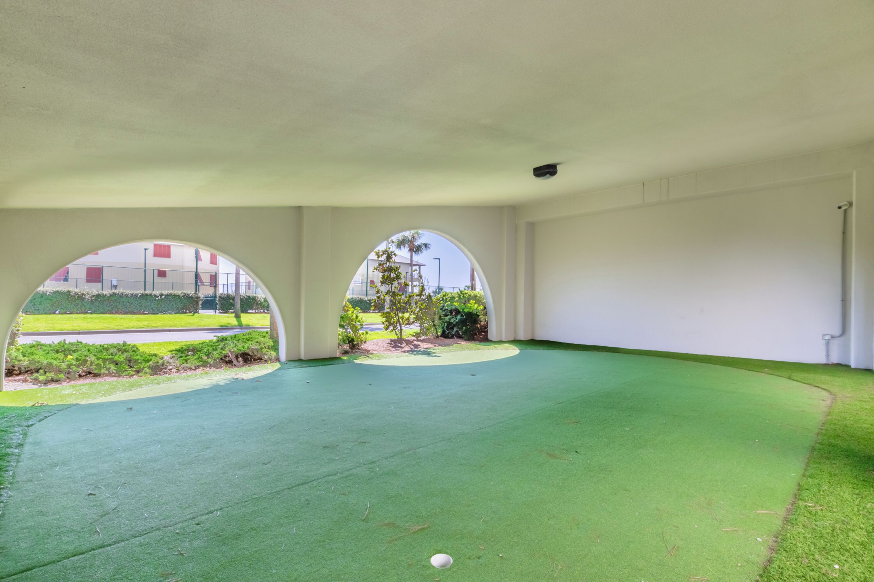 A room with a green artificial turf floor, white walls, and three arched windows.