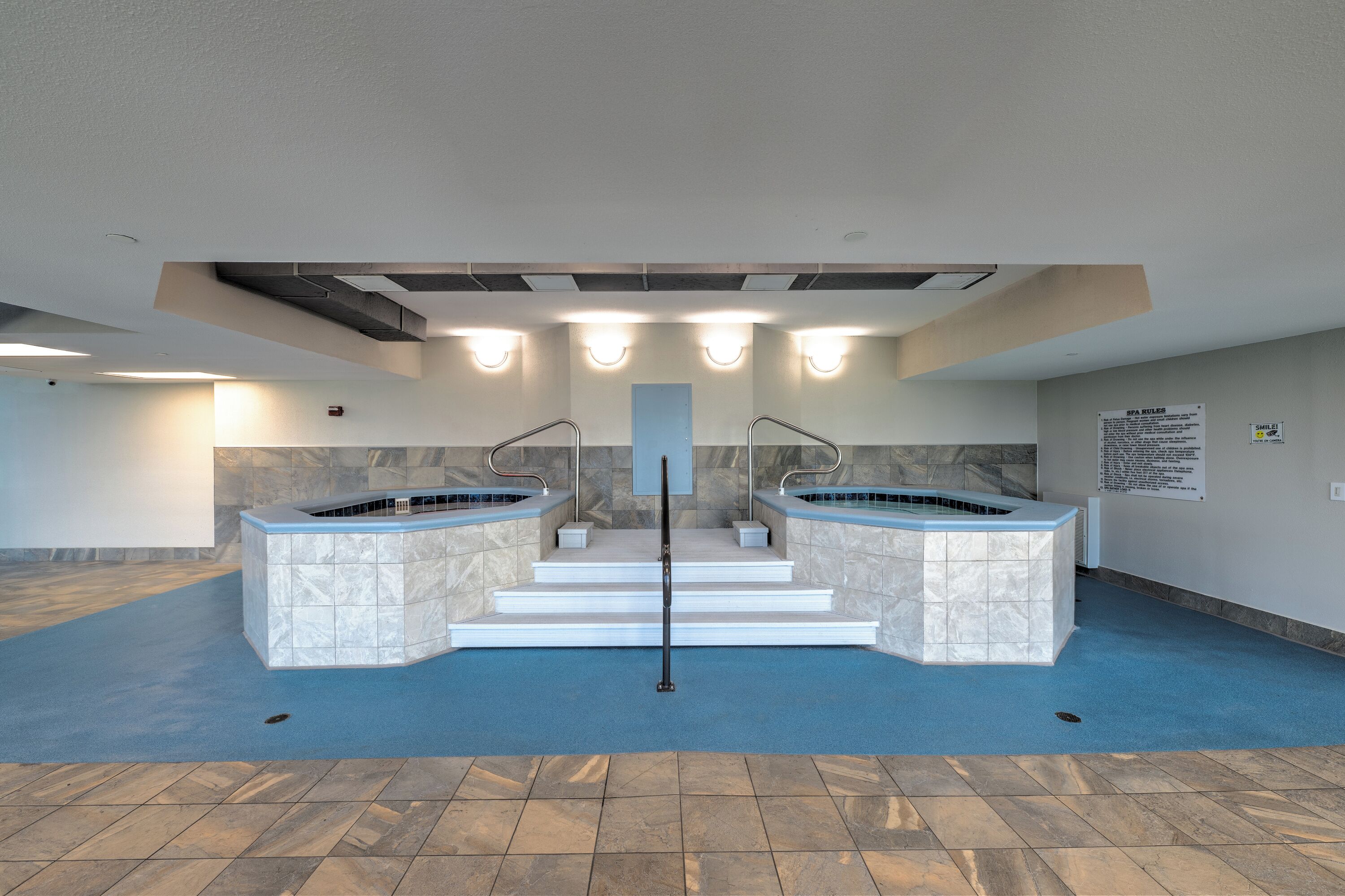 A spa area with two hot tubs, a blue floor, and a sign with spa rules.