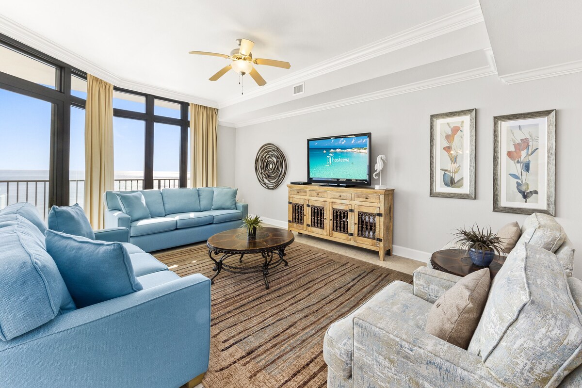 A spacious living room with a large window, a ceiling fan, a flat-screen TV, and a wooden cabinet.