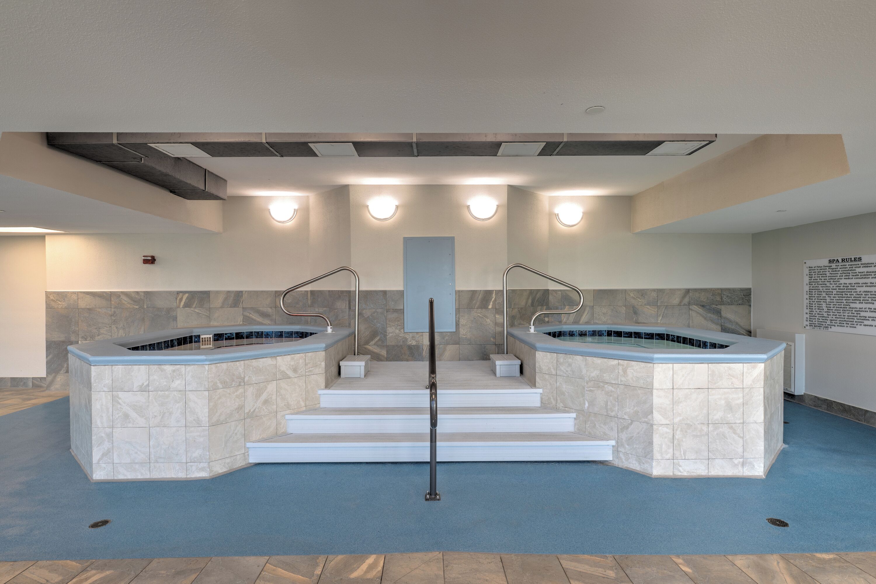 A public spa area with two hot tubs, a central staircase, and a wall with spa rules.