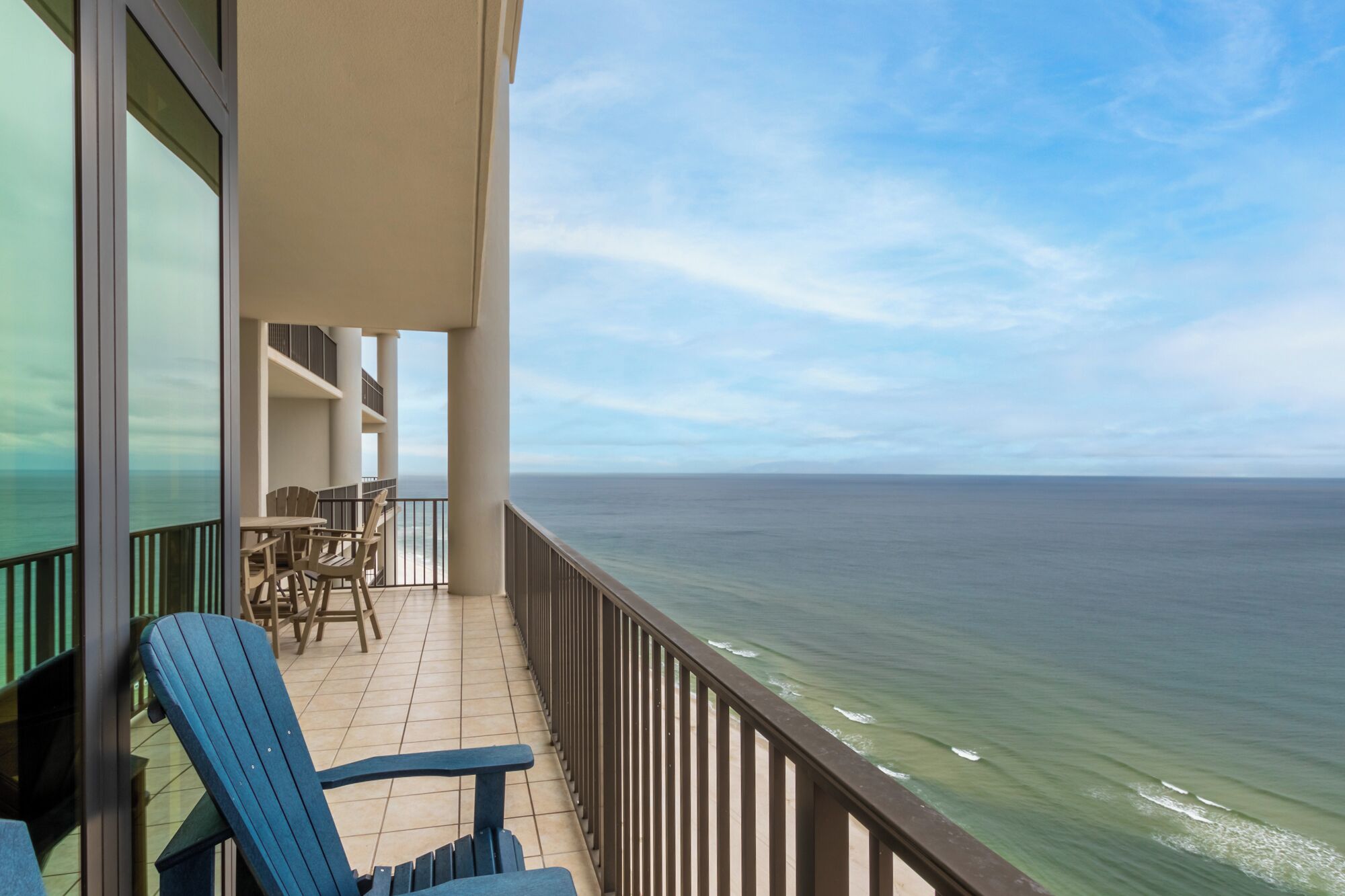 A balcony with a view of the ocean, a blue chair, and a table with chairs.