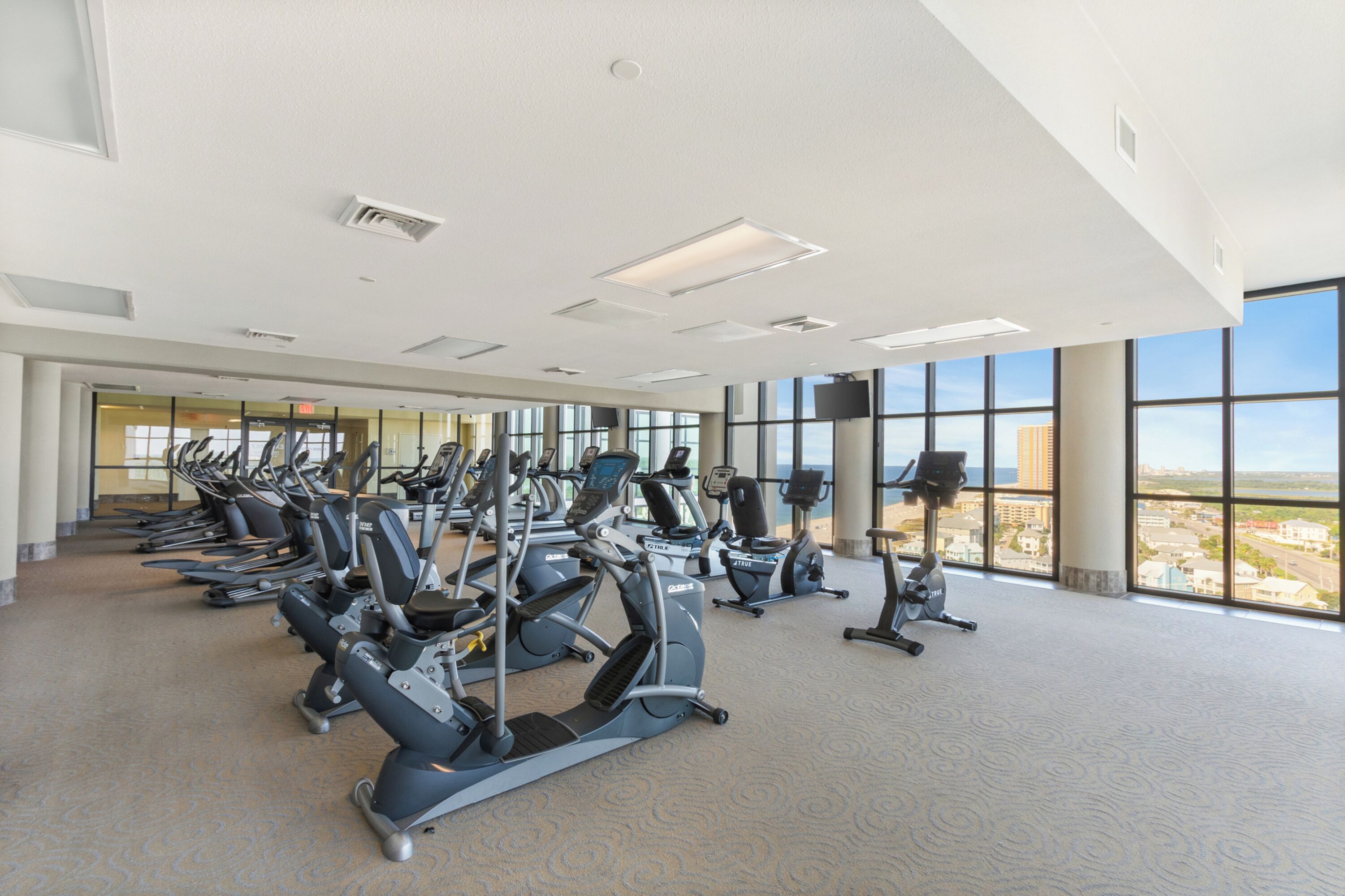 Ein Fitnessstudio mit verschiedenen Cardiogeräten und großen Fenstern, die einen Blick auf die Stadt ermöglichen.
