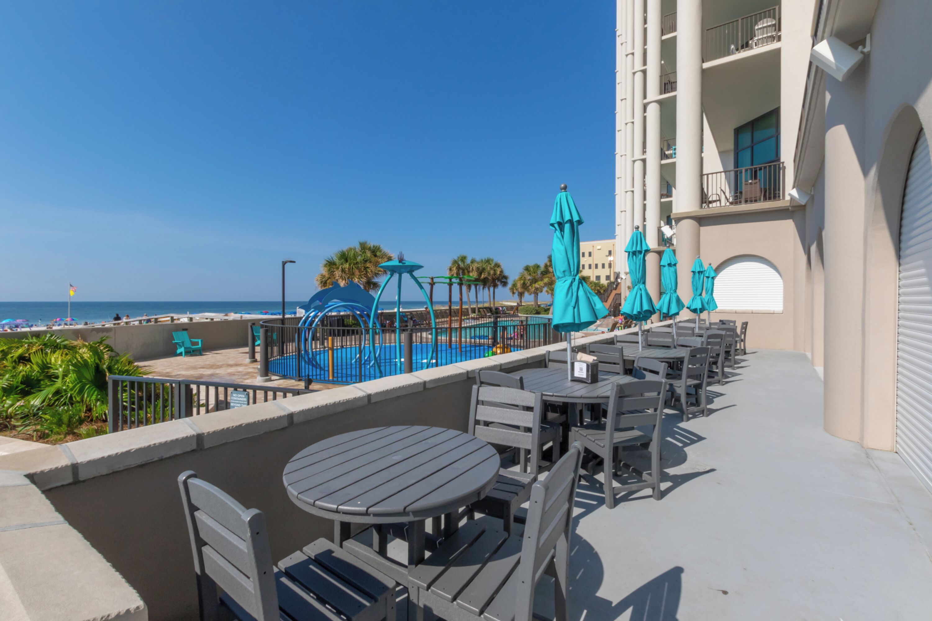 A rooftop pool area with lounge chairs and umbrellas, overlooking the beach and ocean.