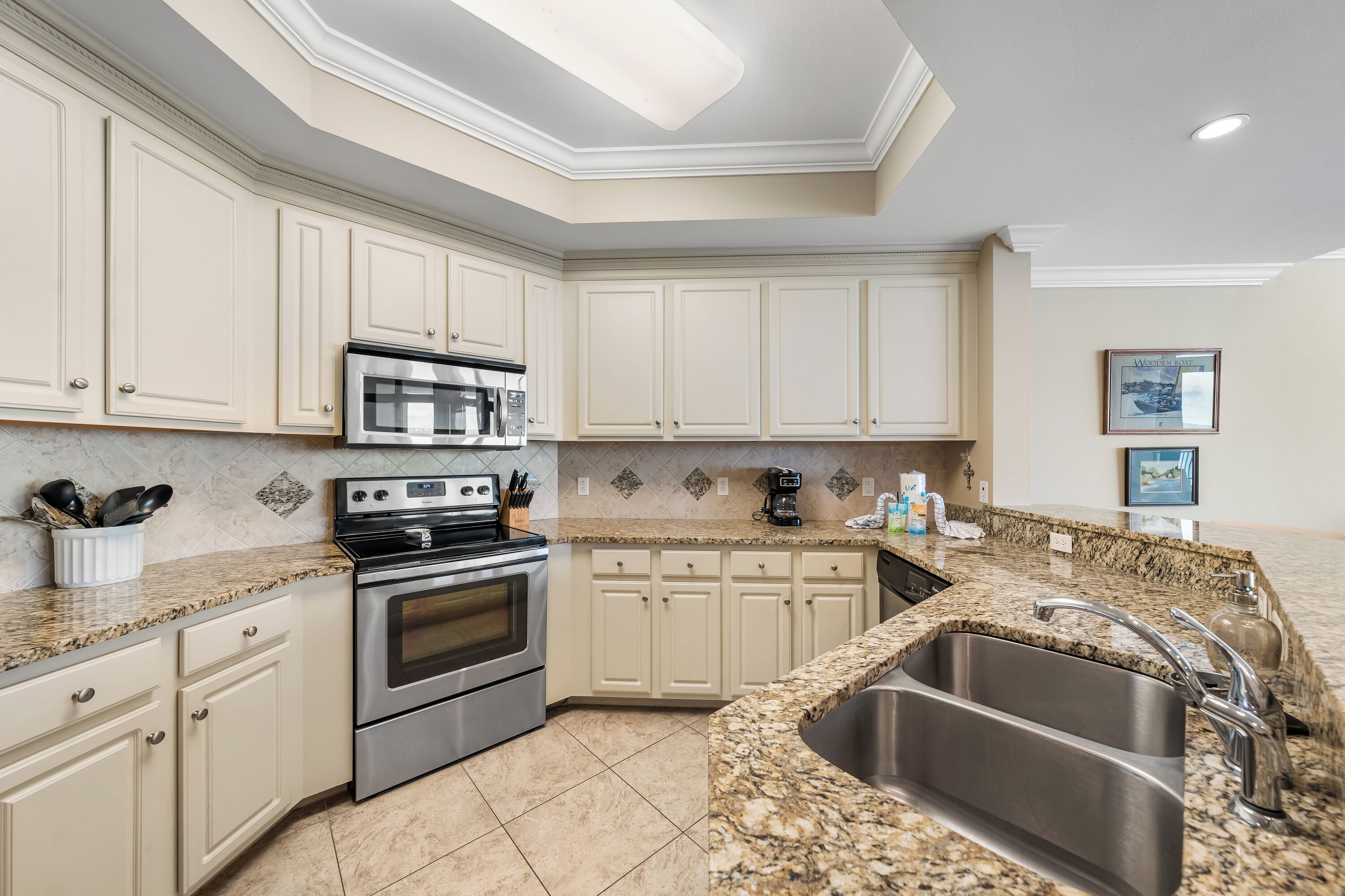 A kitchen with white cabinets, granite countertops, stainless steel appliances, and a large sink.