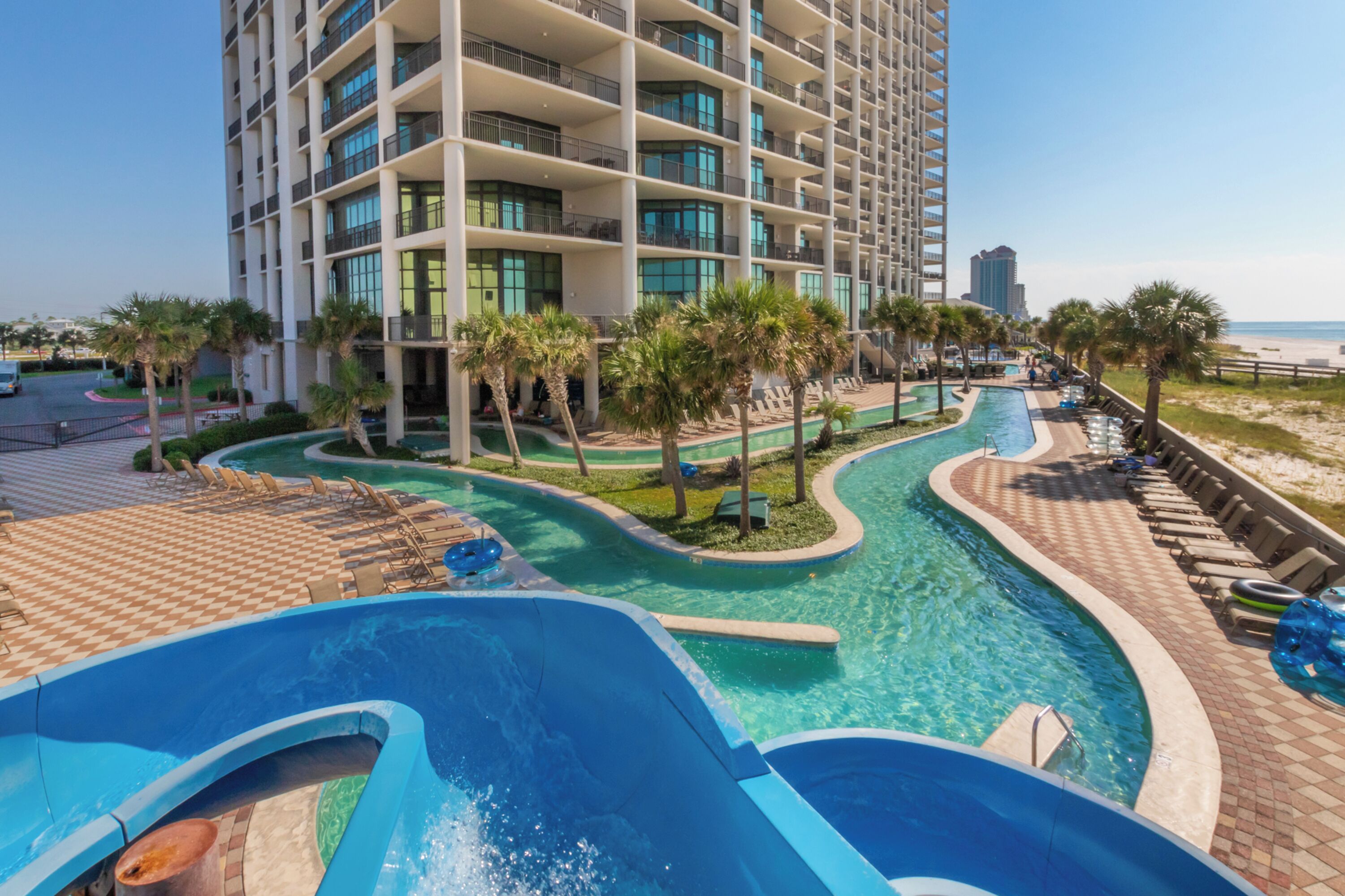 A hotel with a pool area, palm trees, and a view of the beach.
