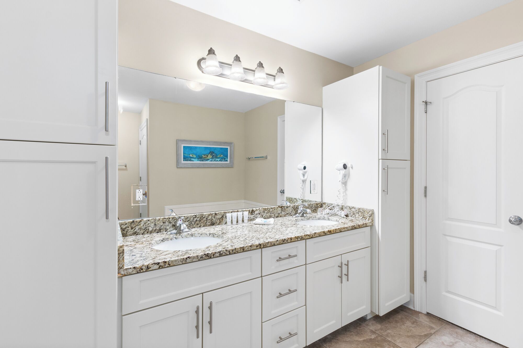 A bathroom with a granite countertop, white cabinets, a large mirror, and a ceiling light fixture.