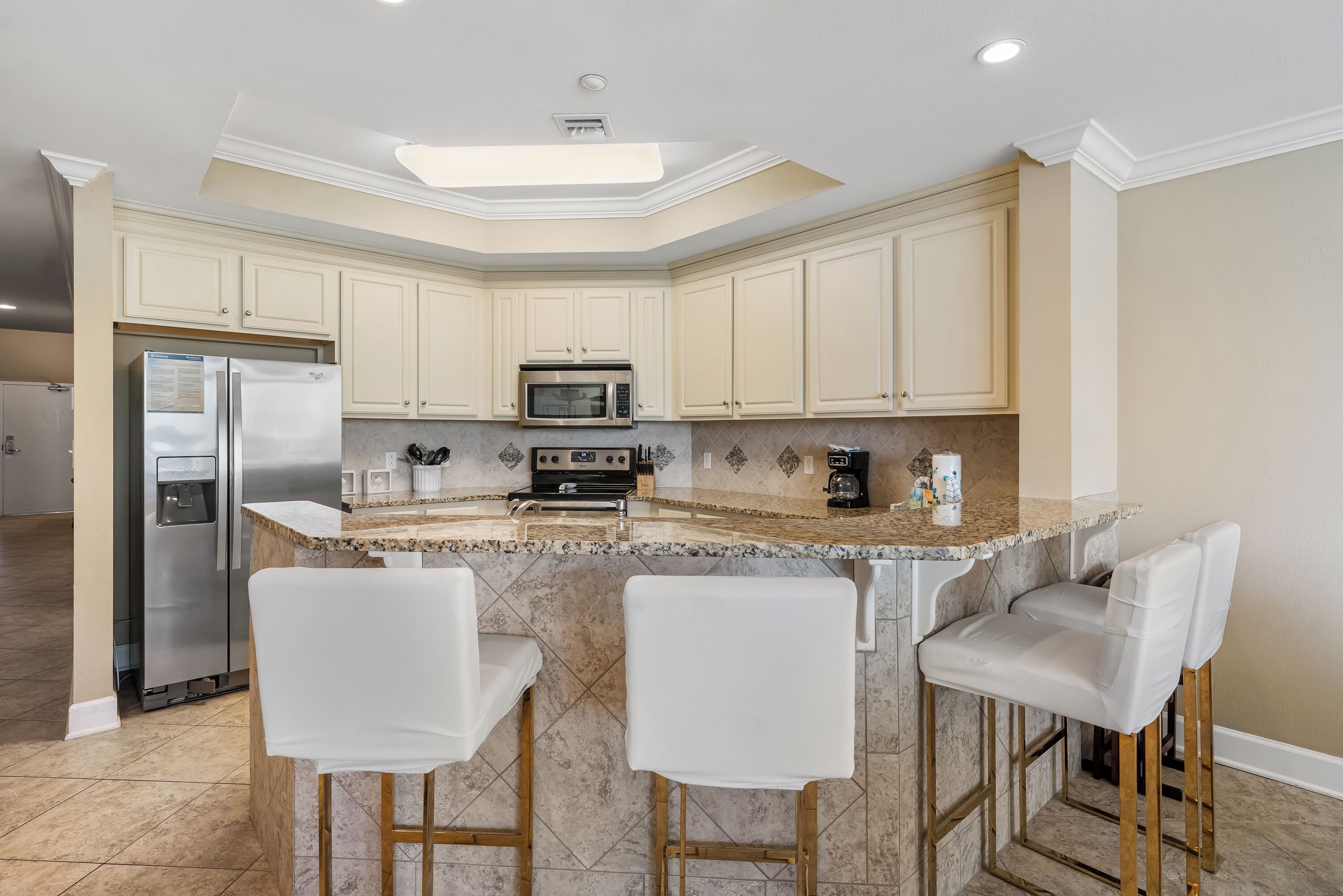 A kitchen with a central island, bar stools, a refrigerator, a microwave, and a stove.