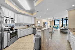 A modern kitchen with stainless steel appliances, white cabinetry, and a large window overlooking the ocean.