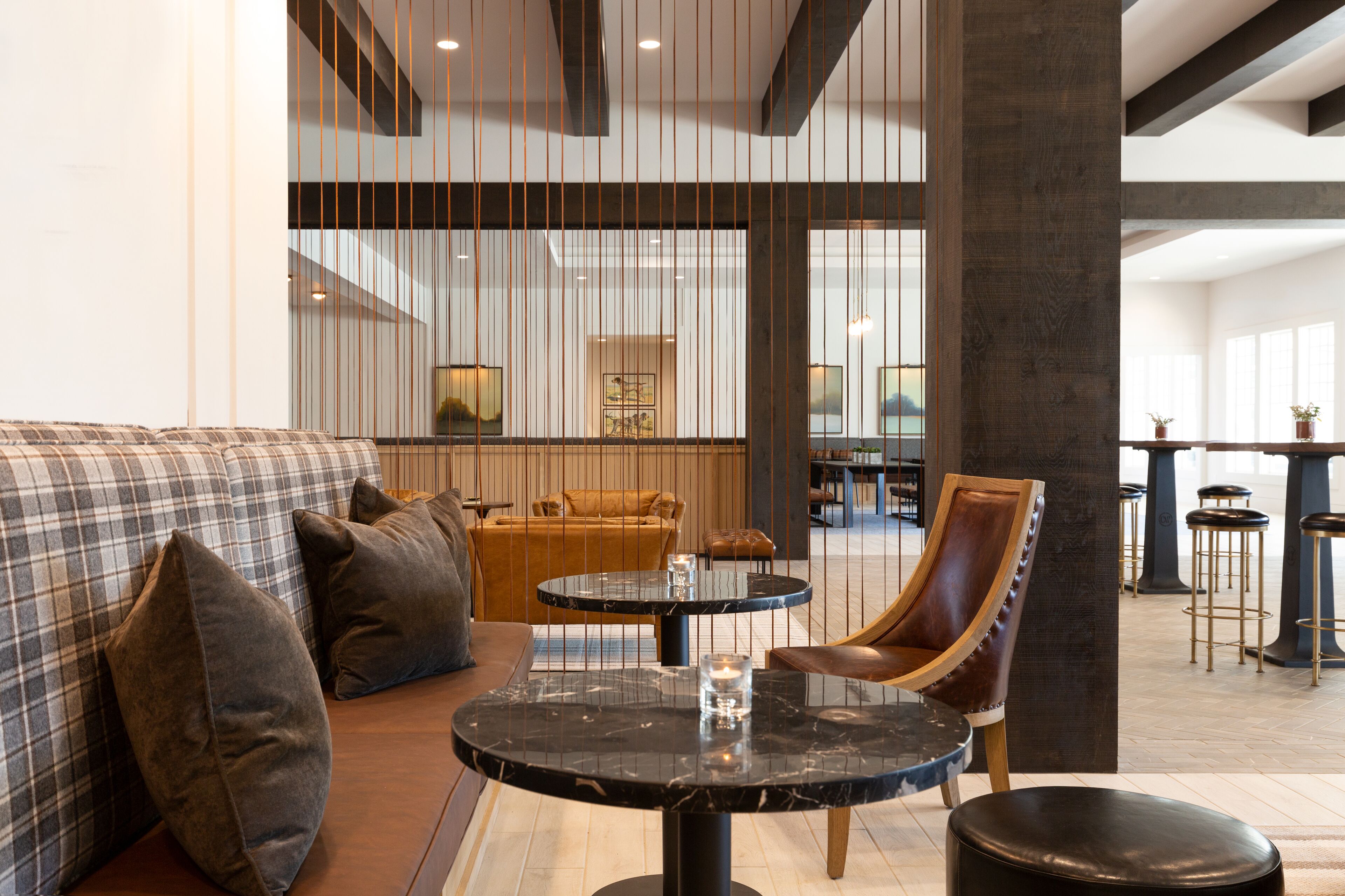 A modern lounge area with a sofa, armchairs, a round table, and a bar area with stools.