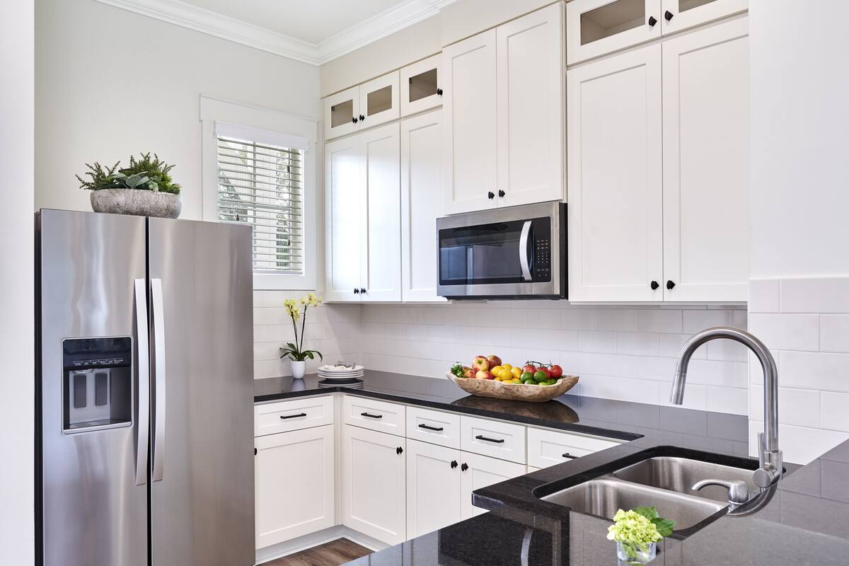 A modern kitchen with white cabinets, stainless steel appliances, a black countertop, and a built-in sink.